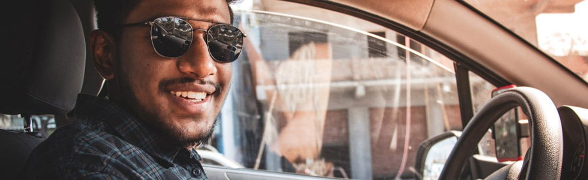 A cheerful man wearing sunglasses driving a vehicle with joy, with car insurance coverage in mind