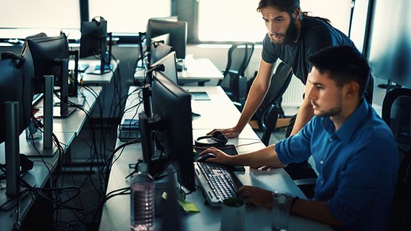 Technology workers problem solve together at a desk station.